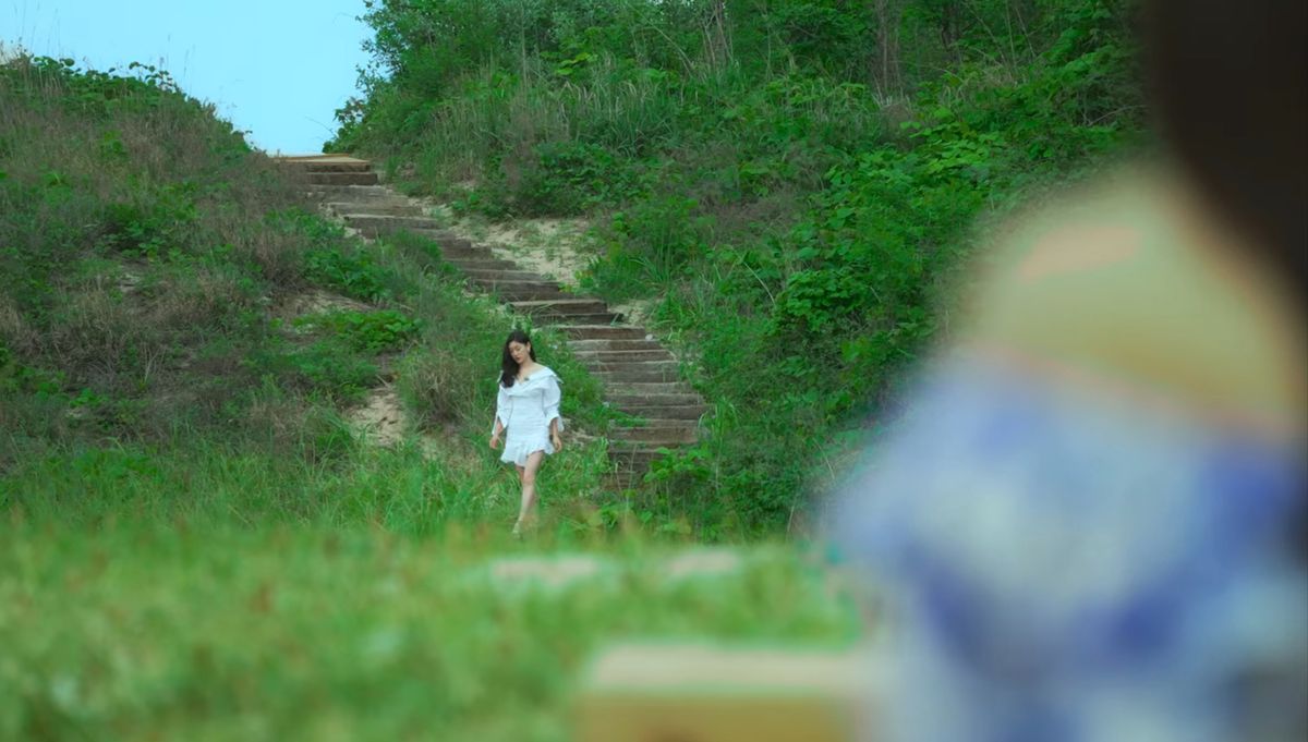 Una donna vestita di bianco scende una lunga scalinata nella seconda stagione di Single's Inferno.