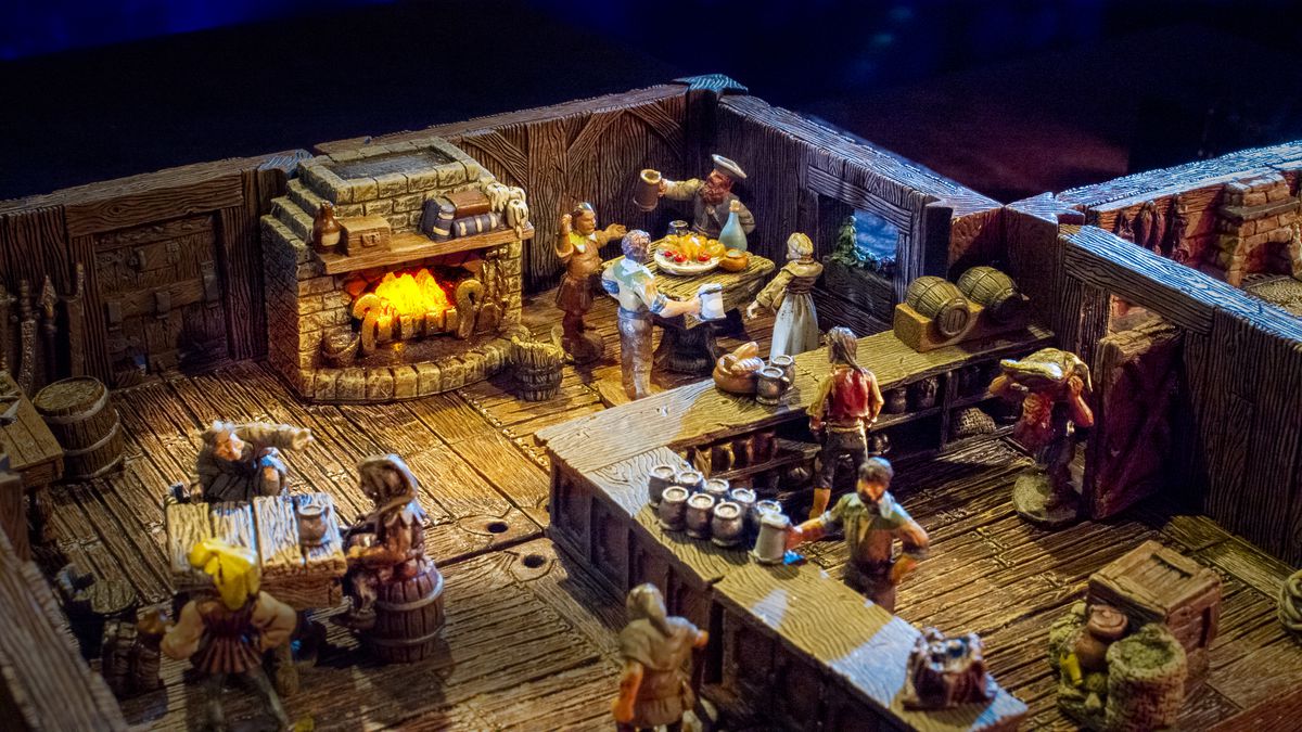 Un'inquadratura ampia di un gruppo di avventori in una taverna medievale. Le birre sono accatastate sul bancone e un pasto viene condiviso nell'angolo, tutto in miniatura, utilizzando il terreno Dwarven Forge.