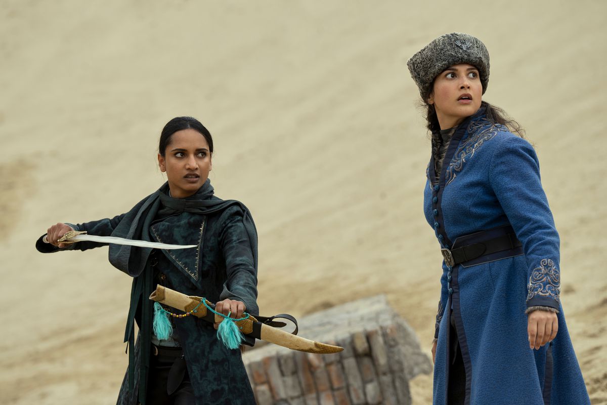 inej che brandisce una spada in un deserto. accanto a lei, Zoya alza lo sguardo