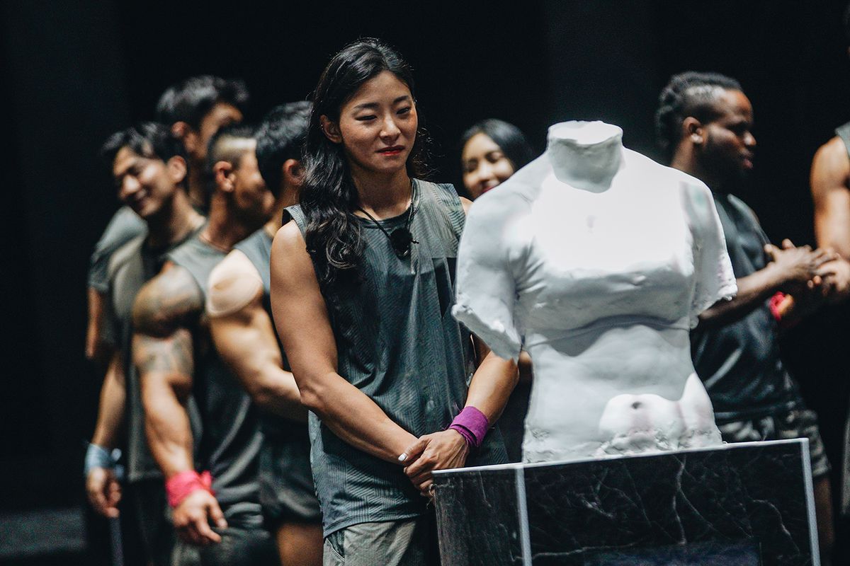 una donna in piedi dietro un torso di gesso decapitato in Physical 100