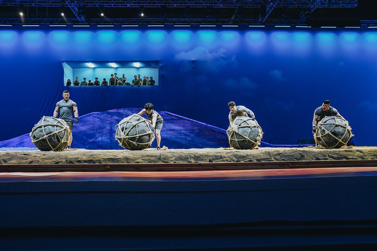 Quattro concorrenti stanno davanti a pesanti massi rotondi ricoperti di corda