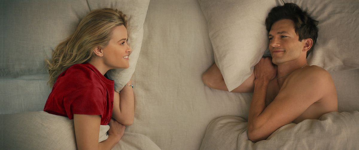 Reese Witherspoon, con indosso un top rosso, e Ashton Kutcher, senza maglietta, si sorridono a letto a Your Place or Mine.
