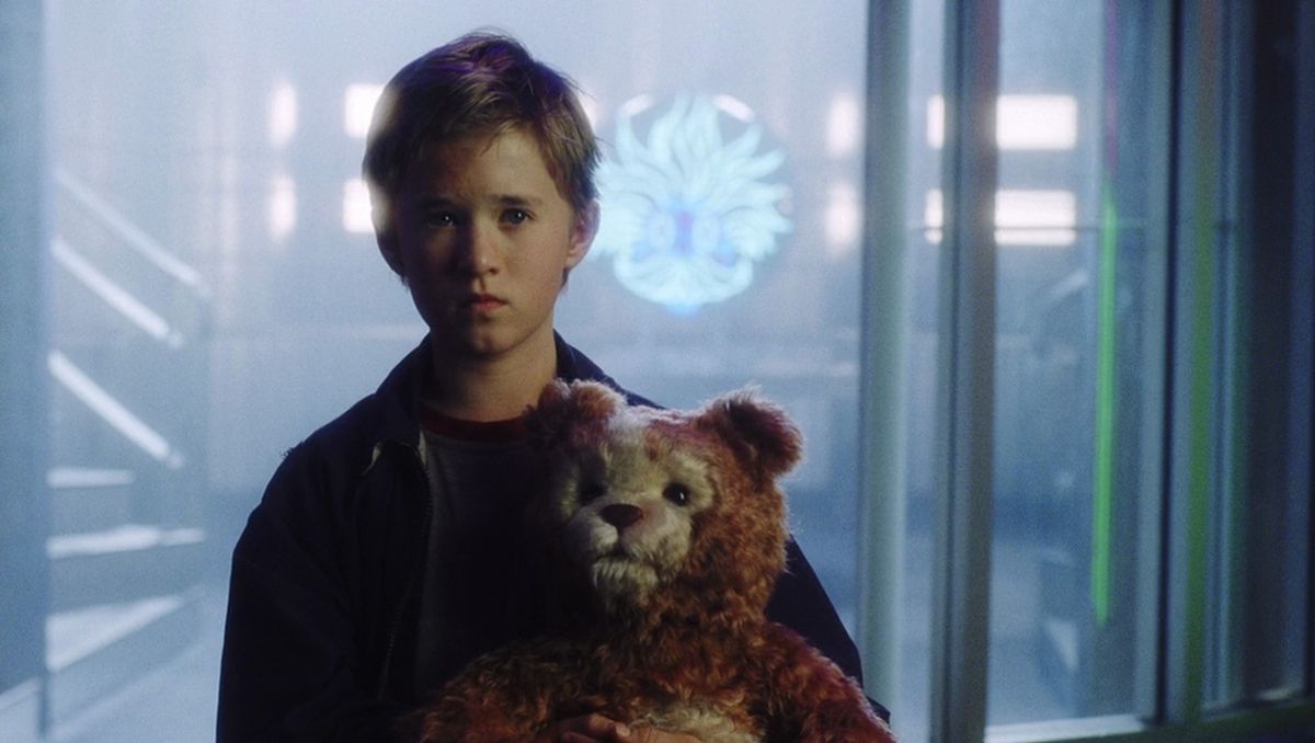 David (Haley Joel Osment) tiene in mano un orsacchiotto di fronte a insegne luminose al neon in AI Artificial Intelligence