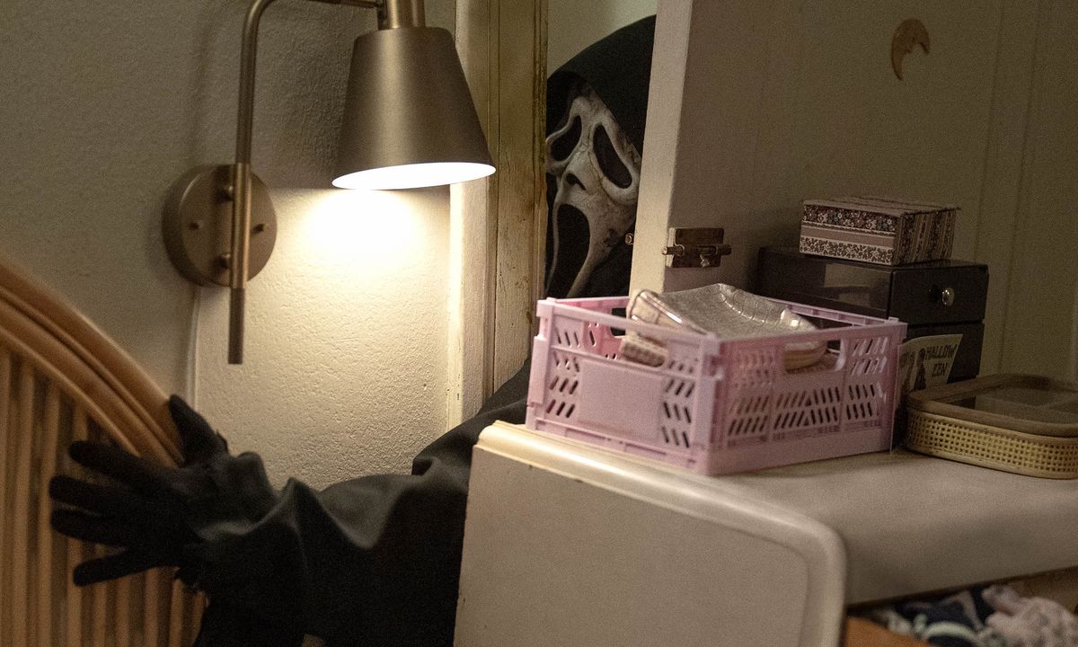 L'assassino mascherato di Ghostface cerca di farsi strada attraverso una porta aperta e bloccata da una cassettiera in Scream VI