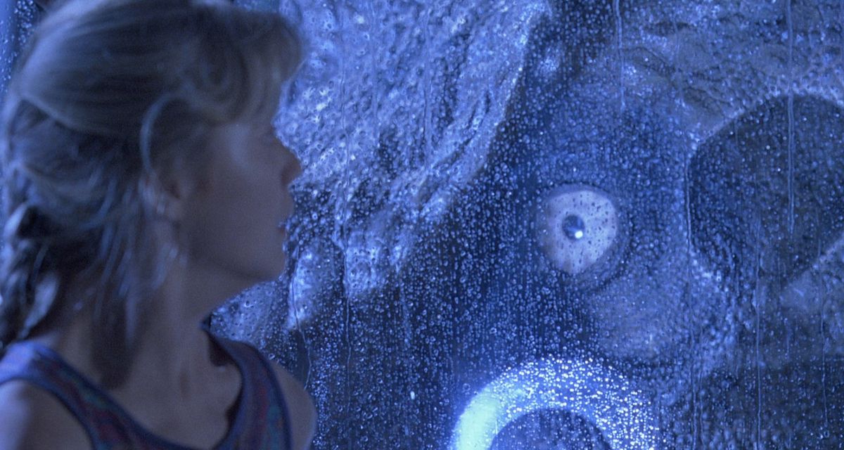 Un T-Rex inzuppato di luce blu guarda dal finestrino di una jeep una ragazza bionda spaventata a Jurassic Park