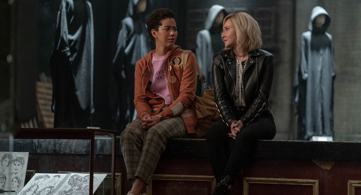 Kirby (Hayden Panettiere) e Mindy (Jasmin Savoy Brown) siedono insieme su un palco con le gambe che penzolano dal bordo mentre manichini in abiti grigi con cappuccio incombono dietro di loro in Scream VI