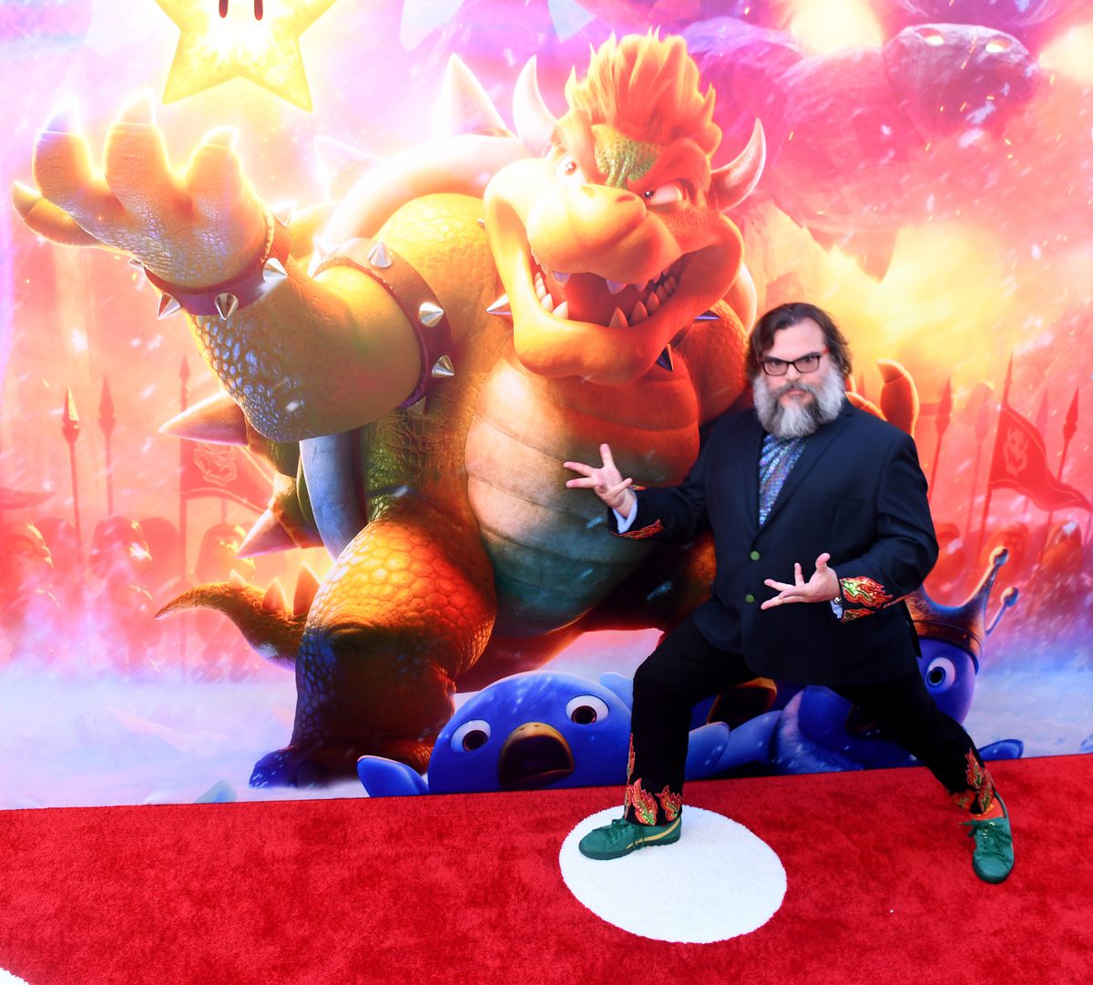 Jack Black posa, con mani simili ad artigli, sul tappeto rosso alla premiere di Los Angeles di The Super Mario Bros. Movie. Indossa un abito con le punte sulla schiena di Bowser e una maglietta con una stampa olografica a scaglie di lucertola.