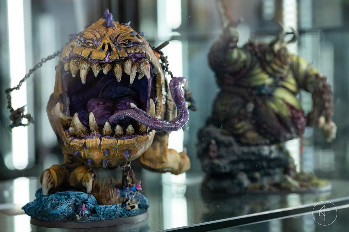A giant yellow and purple monster on display. Behind it is a virulent green demon. Both miniatures use a strong base and layered colors to draw attention to the different details and textures on the creatures — from worn teeth to cracked lips.