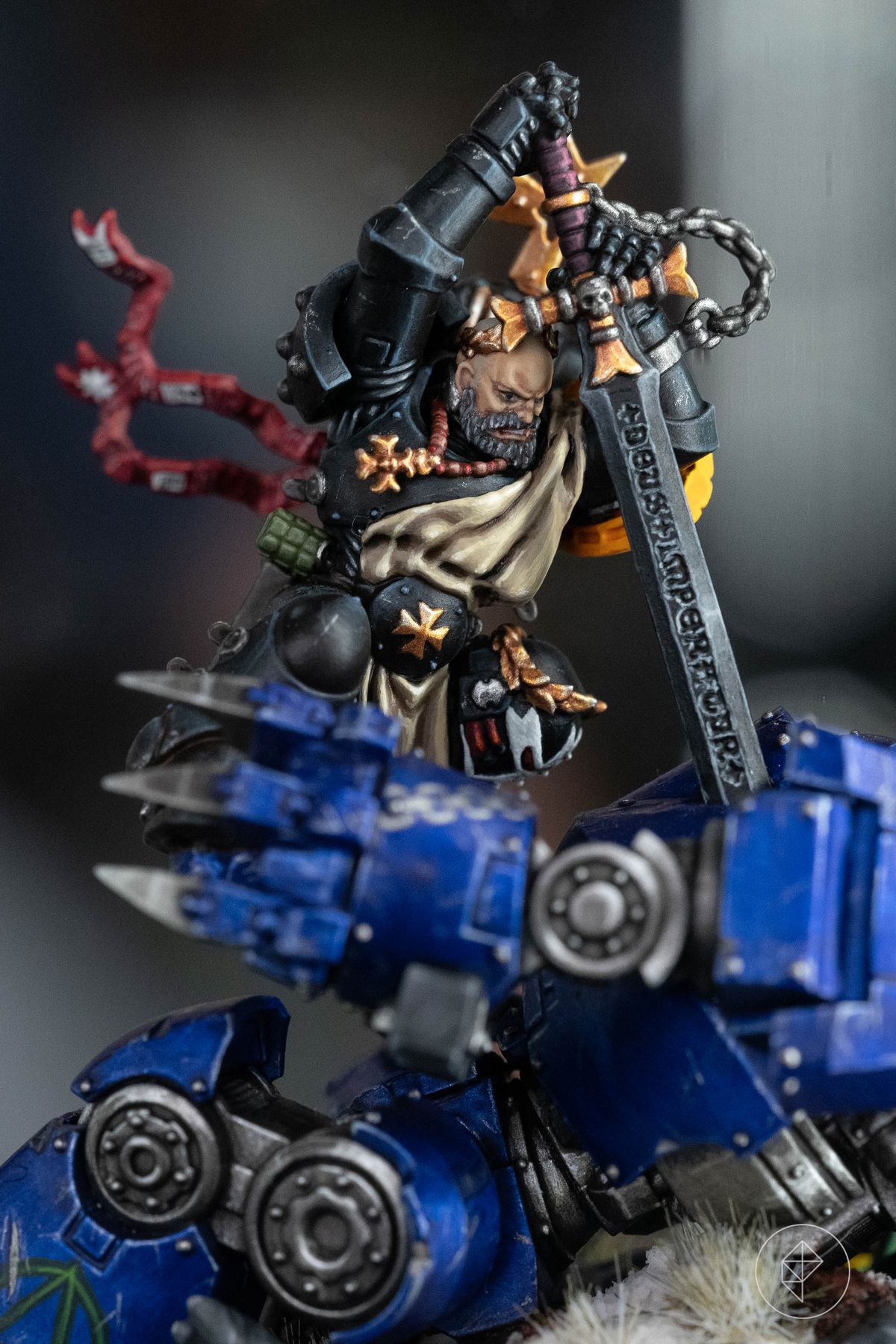 A Black Templars space marine plunges a sword into a dreadnought miniature, ribbons streaming behind him. His sword is inlaid with the words “Deus Imperator.”