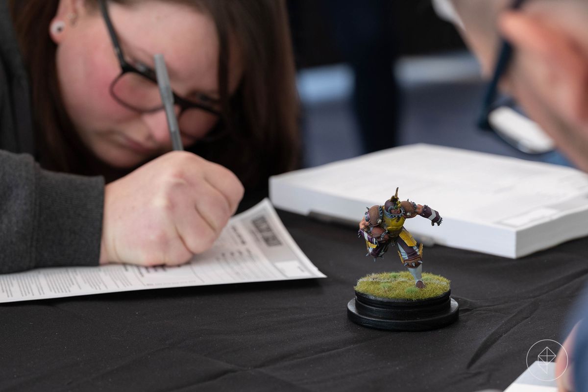 A Golden Demon participant signs a document, handing over their miniature to be judged.