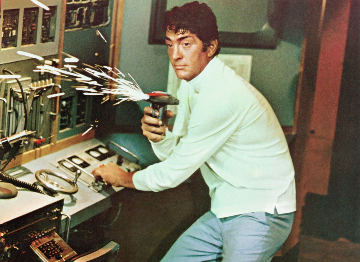 Matt Helm spara con una pistola futuristica che si illumina di scintille mentre colpisce un interruttore su un pannello di controllo