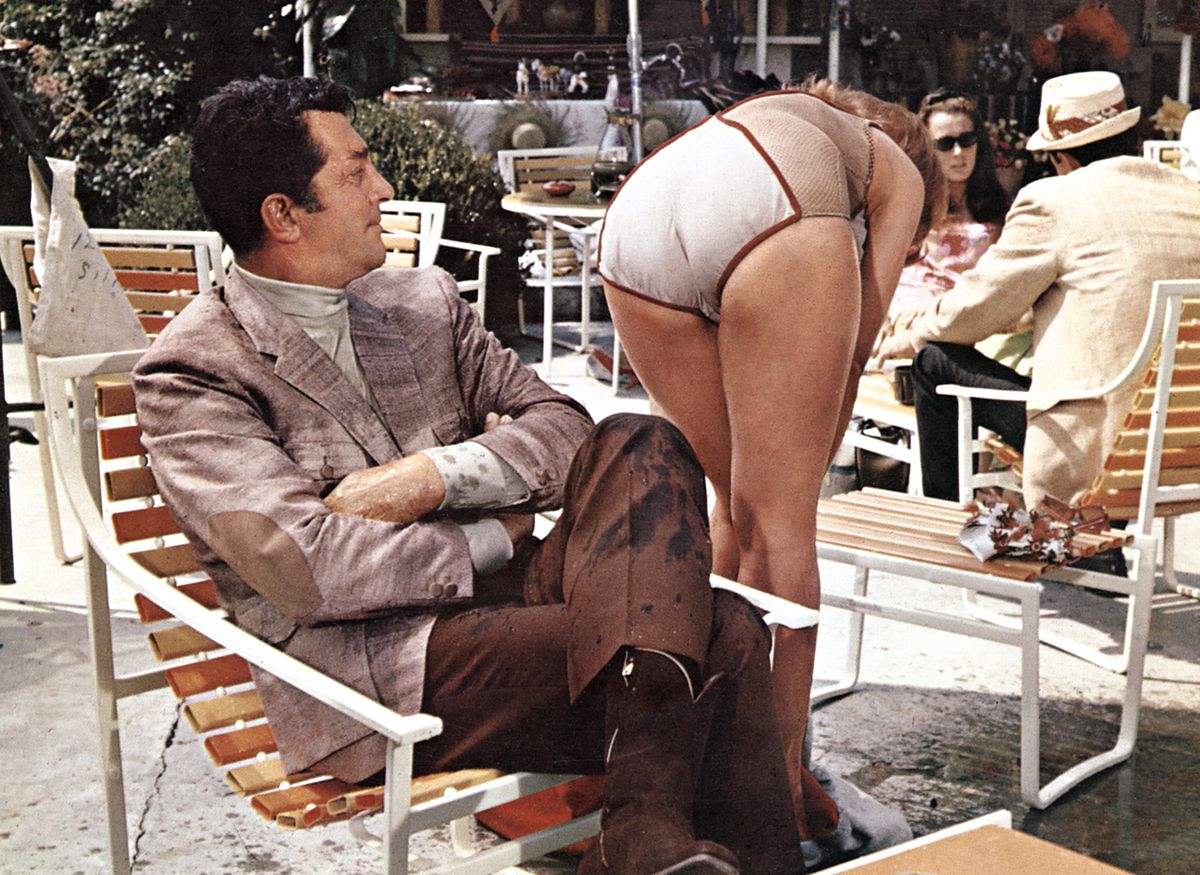 Una donna in costume da bagno si china davanti a Matt Helm che le guarda il sedere con aria di approvazione