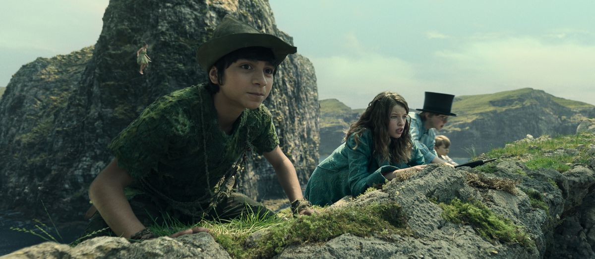 Peter Pan (Alexander Molony), Wendy (Ever Anderson), John Darling (Joshua Pickering) e Michael Darling (Jacobi Jupe) si accovacciano in cima a una cresta rocciosa coperta di muschio, guardando oltre il bordo in Peter Pan e Wendy