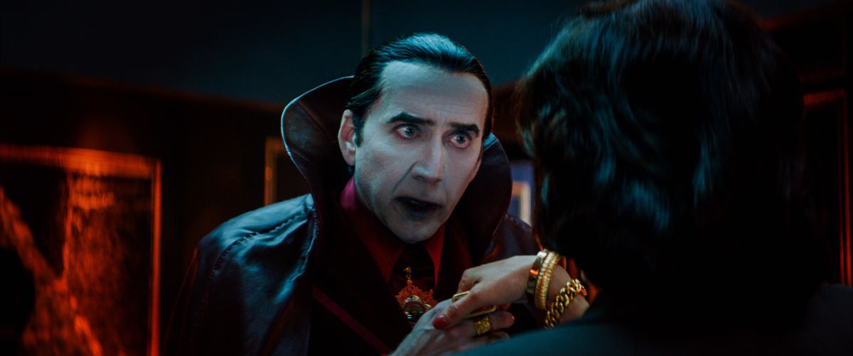 Nicolas Cage nei panni di un film molto tradizionale Il conte Dracula (pelle pallida come la carta, capelli neri lisci con la punta di una vedova, mantello nero con un enorme collo alto, sguardo affamato negli occhi) prende la mano di una donna con la schiena alla telecamera a Renfield