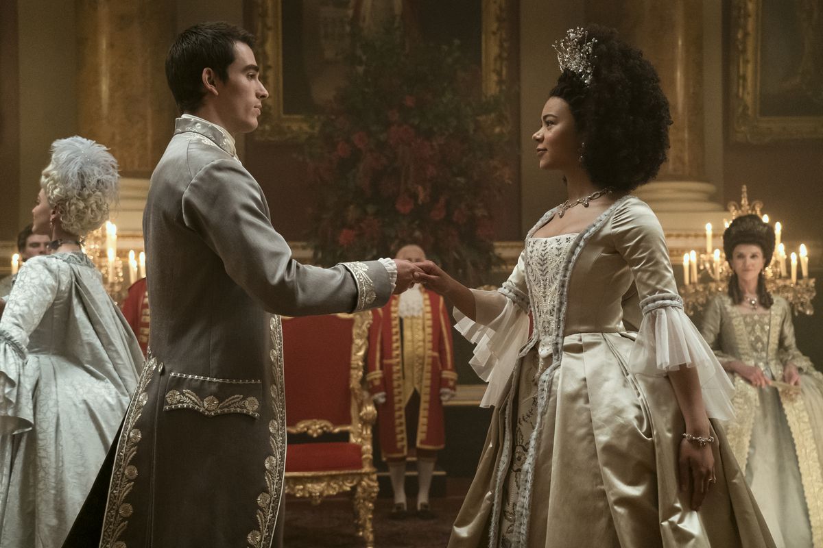King George, un giovane alto dai capelli scuri, tende una mano alla regina Charlotte, una giovane donna con un impressionante afro