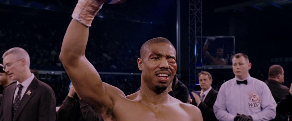 Michael B. Jordan nei panni di Adonis Creed che alza il pugno e sorride con l'occhio sinistro gonfio in Creed.