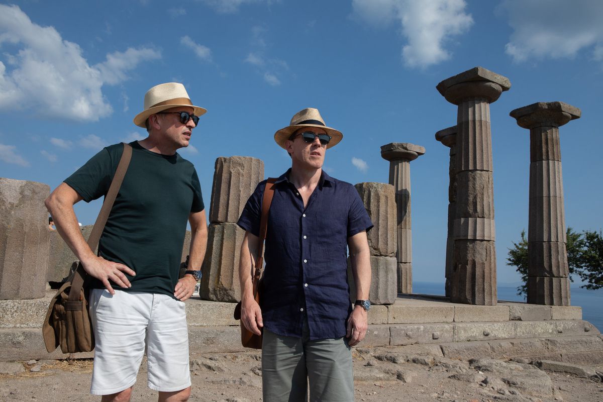 the two men stand among a set of columns