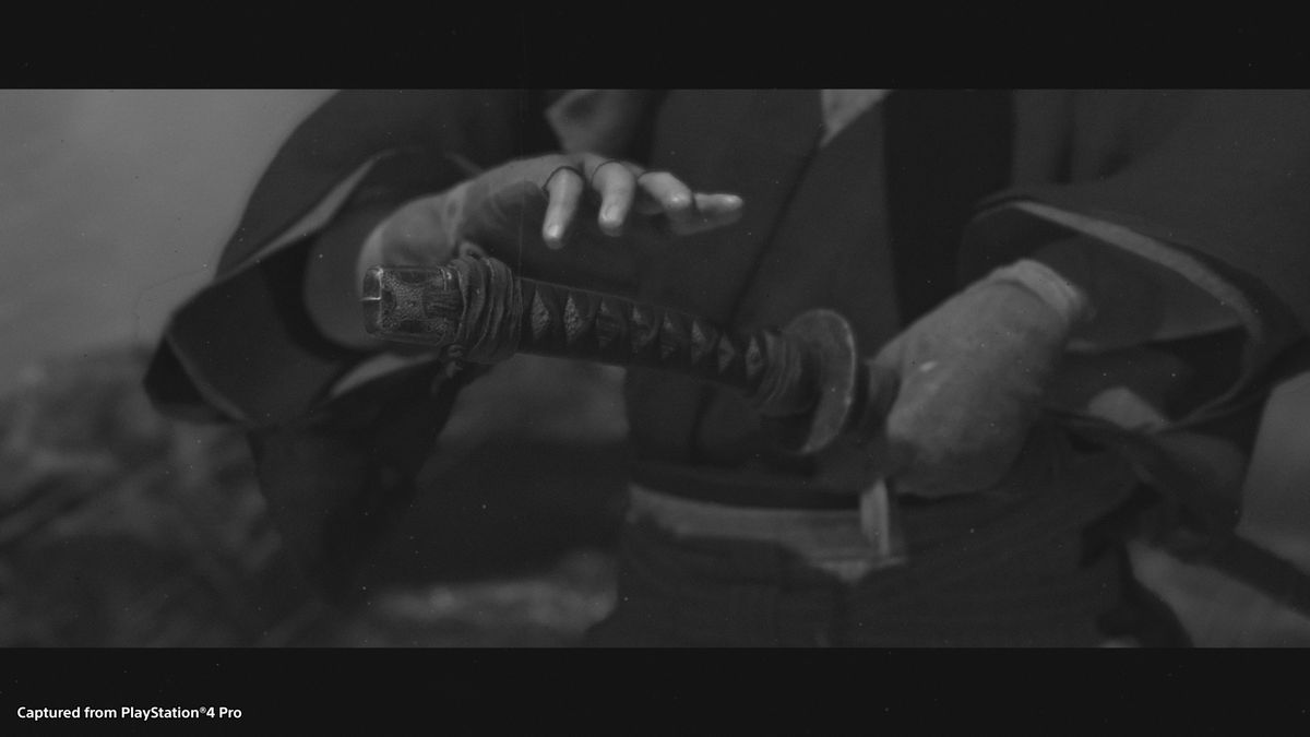 La mano di un samurai prende la sua spada in uno screenshot in bianco e nero di Ghost of Tsushima