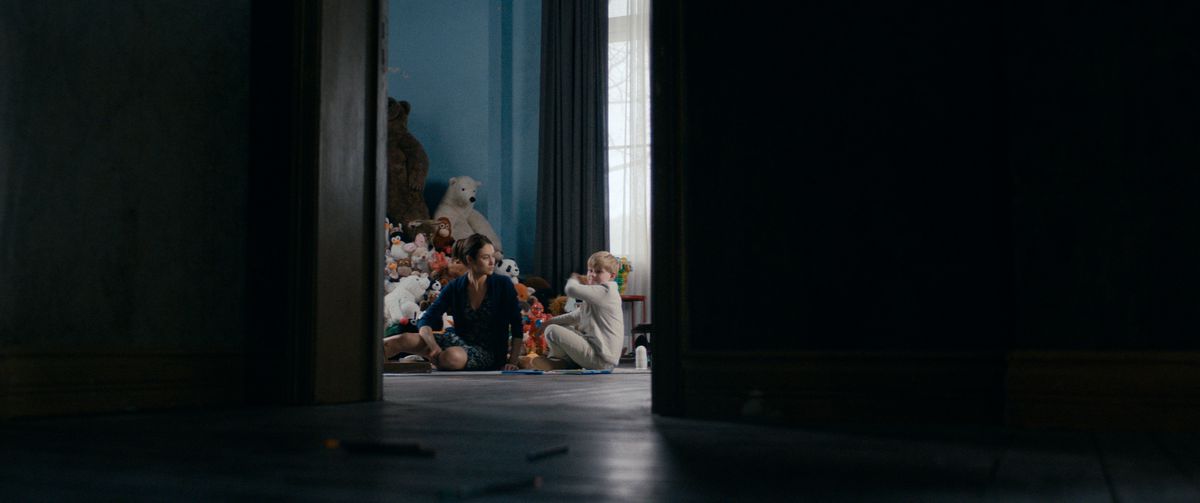 Olga Kurylenko siede con il suo bambino soprannaturale appena acquisito in The Room. 