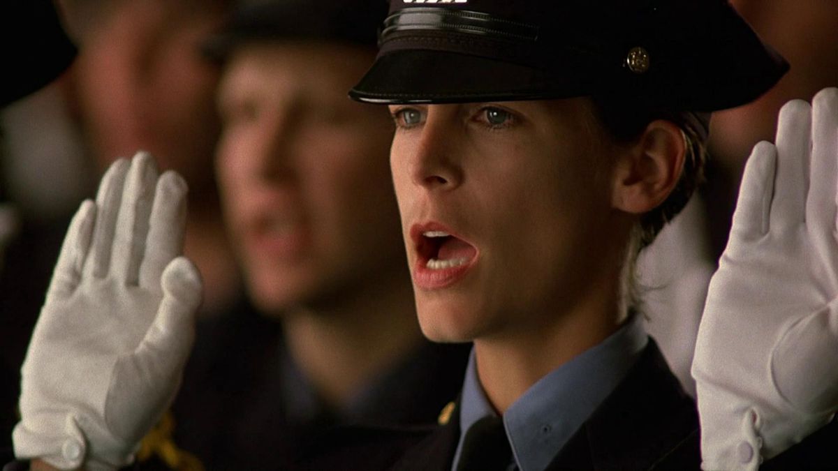 Jamie Lee Curtis, in uniforme della polizia e guanti bianchi, presta giuramento in un gruppo di altre forze dell'ordine in Blue Steel.