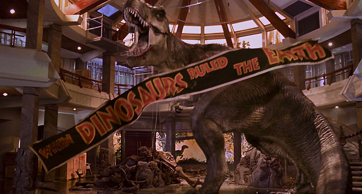 fine del jurassic park: il t-rex sconfigge i rapaci nell'atrio del jurassic park mentre uno striscione 