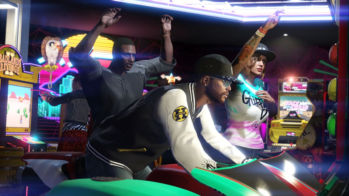 un uomo di colore che gioca a un gioco di corse arcade mentre due amici guardano l'aggiornamento Diamond Casino Heist di Grand Theft Auto Online