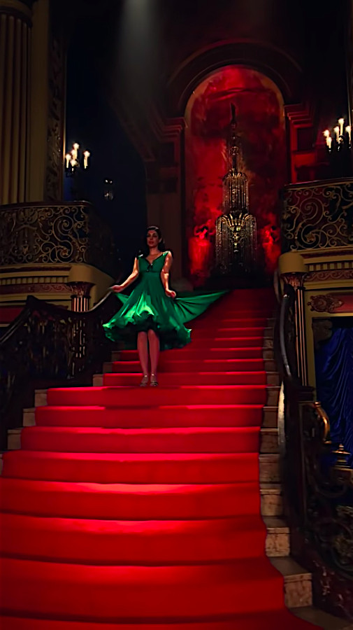 Una donna con un abito verde brillante si trova su una scala rosso vivo in 