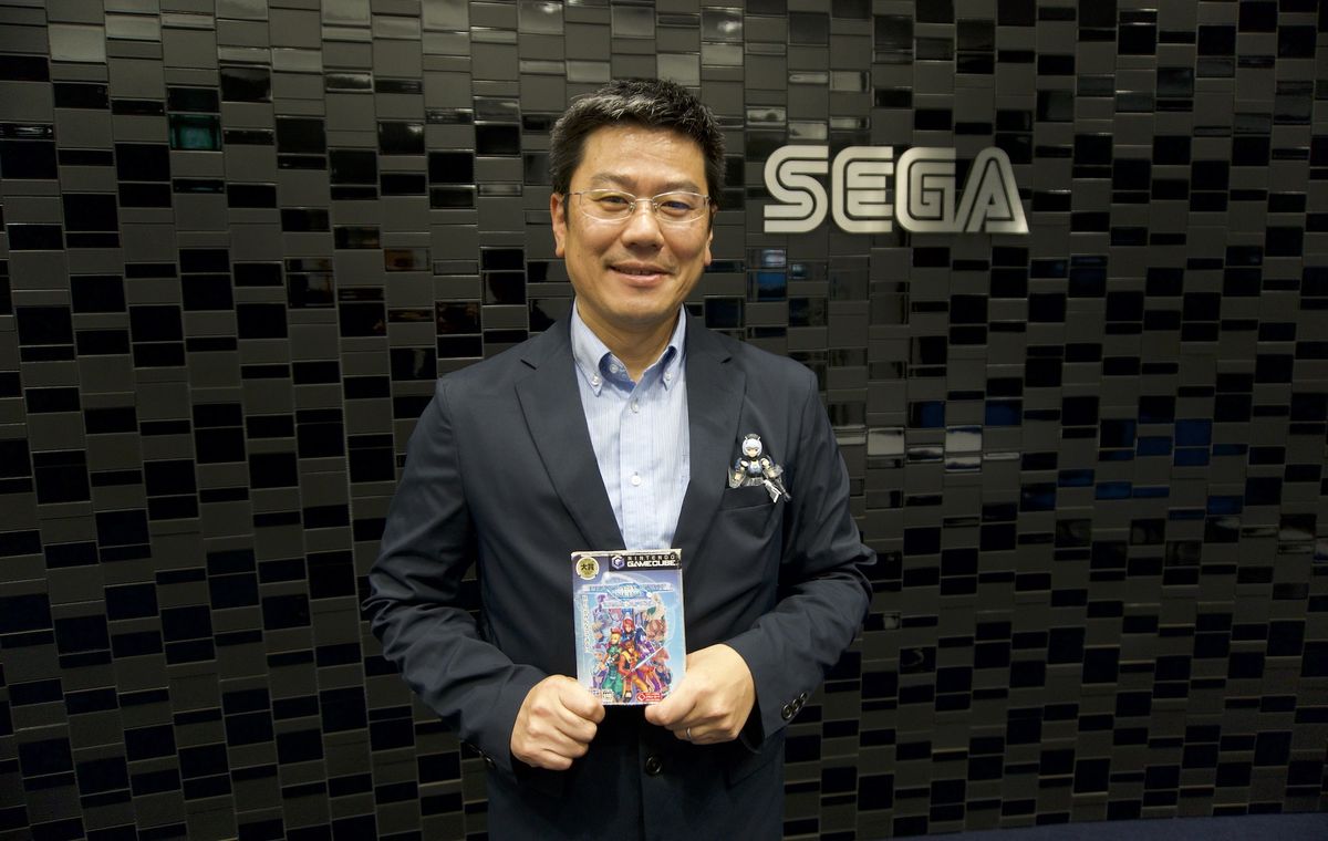 Takao Miyoshi tiene una copia GameCube di Phantasy Star Online di fronte a un muro con sopra il logo Sega