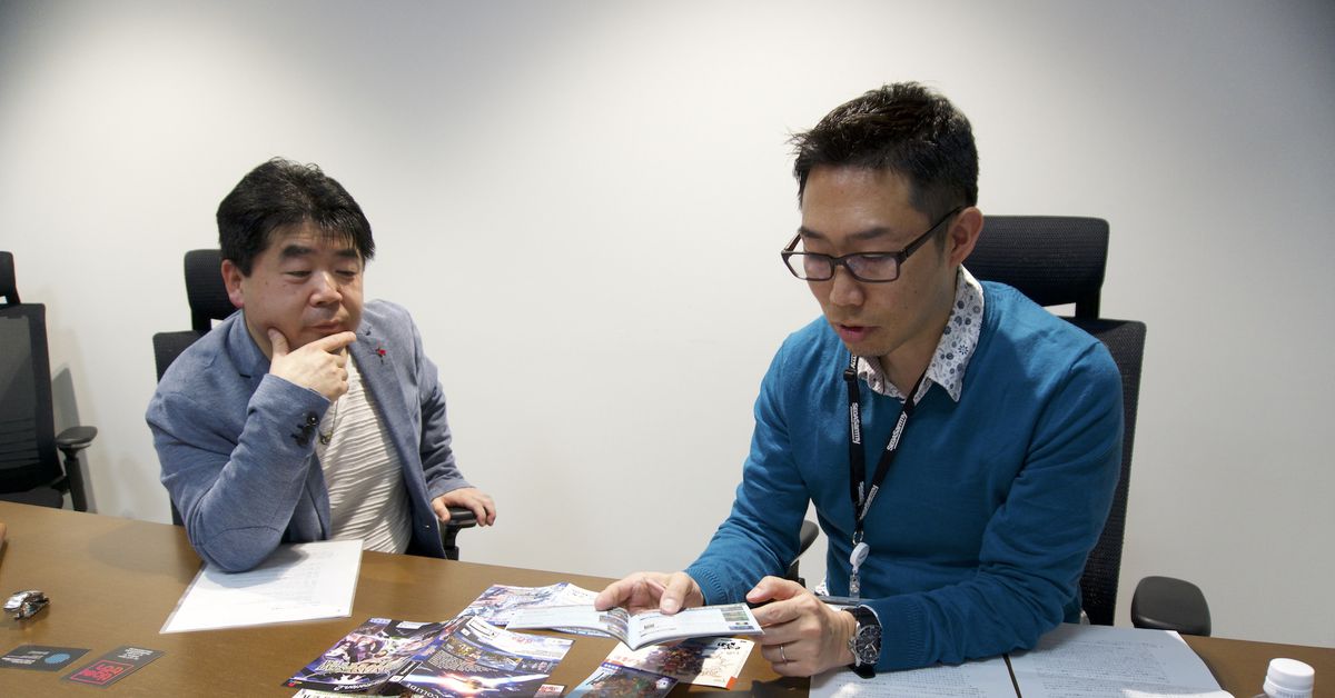 Due sviluppatori di giochi esaminano un tavolo coperto da diverse versioni di Phantasy Star Online