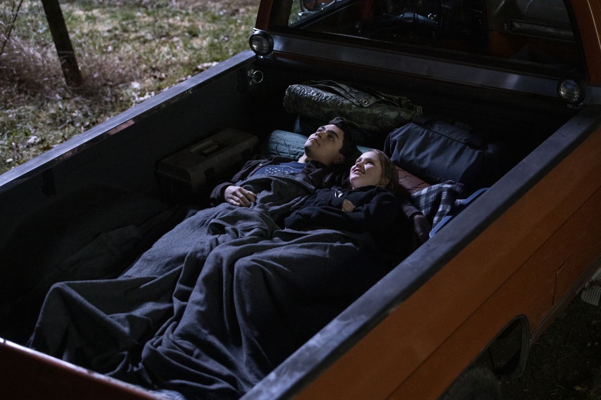 Adam Irigoyen e Talitha Eliana Bateman giacciono sotto una coperta nel pianale di un camion e guardano il cielo notturno nella serie di Netflix Away.