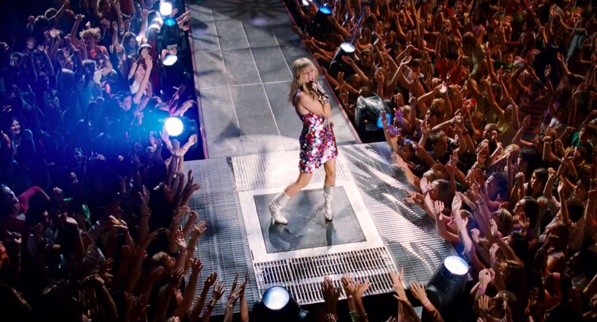 Miley Cyrus nel ruolo di Hannah Montana si esibisce su un palco circondato da una folla ad Hannah Montana