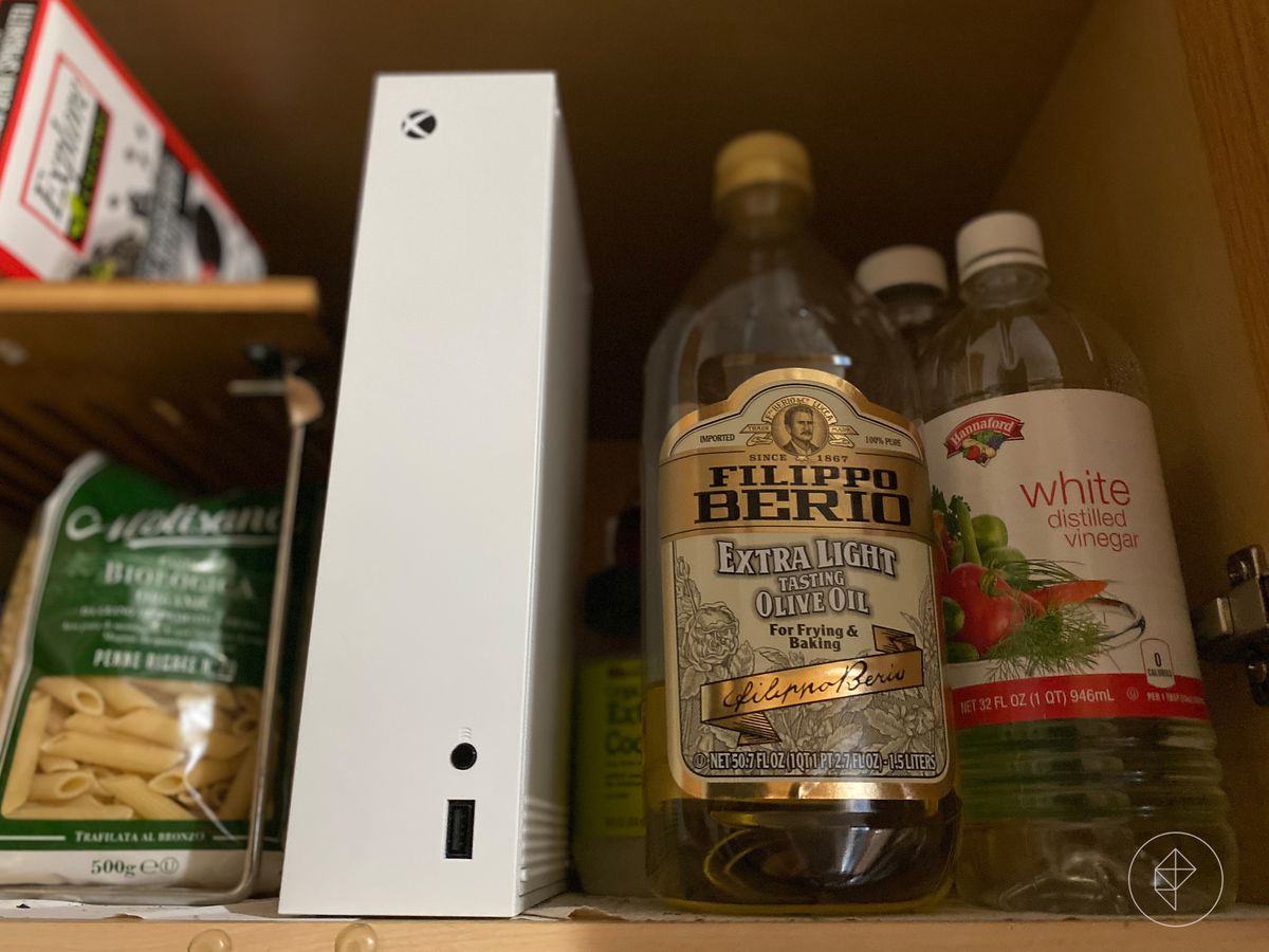 Foto di una console Xbox-S accanto a una bottiglia di olio d'oliva su uno scaffale della cucina