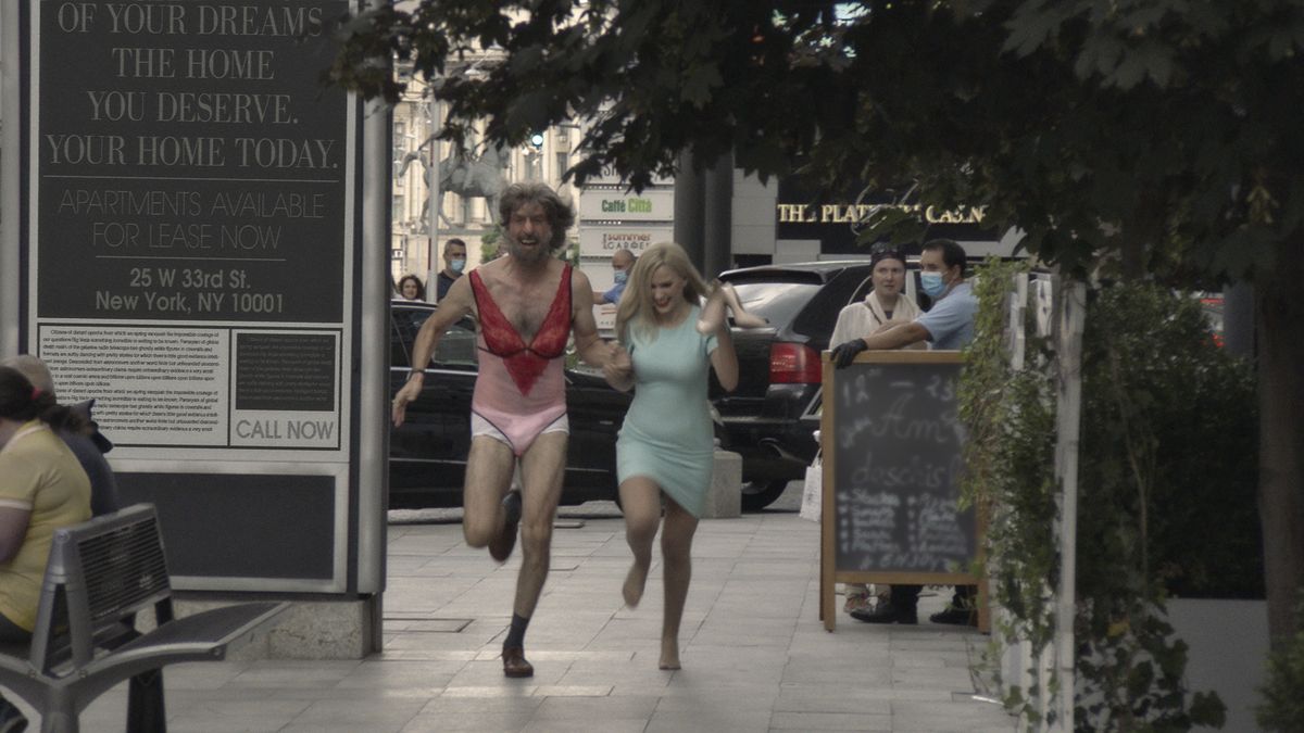 Sacha Baron Cohen, in lingerie and a fake beard and wig, runs through the streets with Maria Bakalova in Borat Subsequent Moviefilm