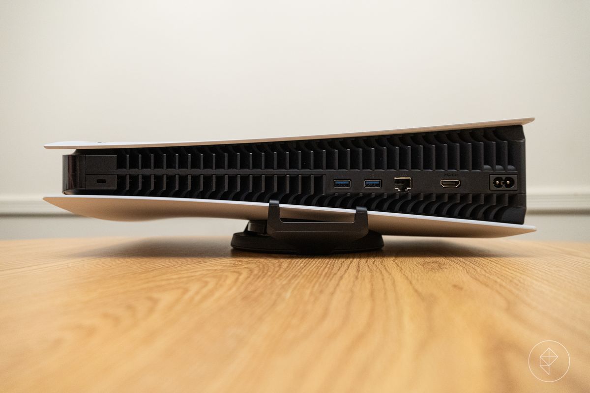 la PlayStation 5 adagiata nel suo orientamento orizzontale su un tavolo di legno, vista da dietro, con i ganci del supporto visibili