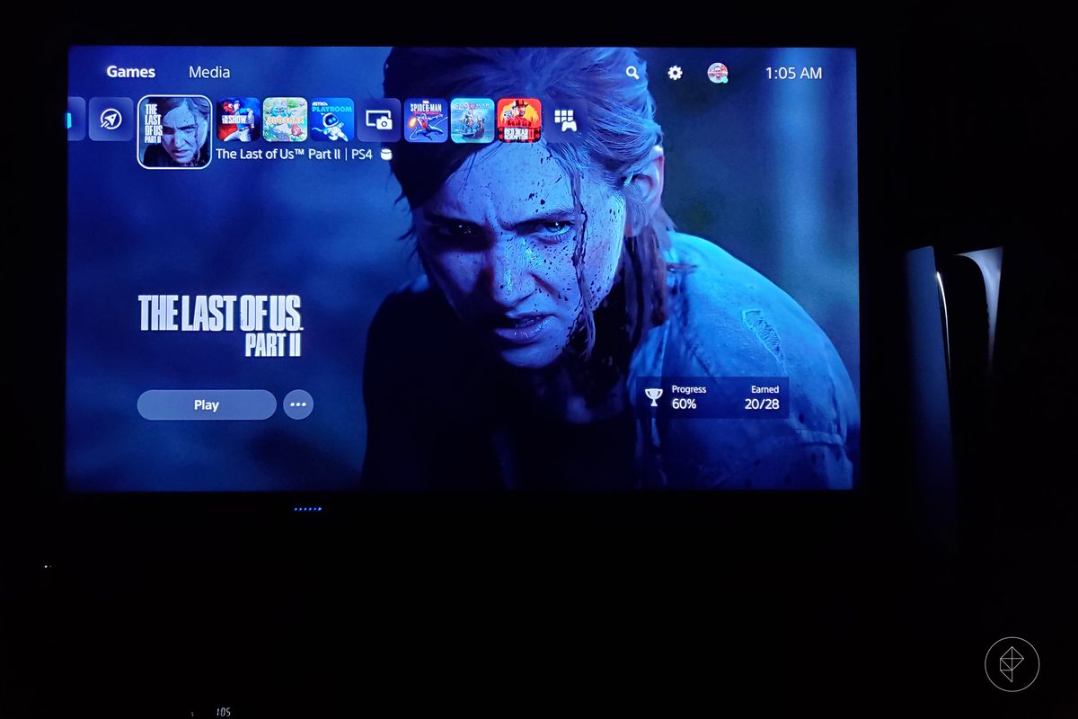 the PlayStation 5 standing vertically to the right of a TV showing the PS5 dashboard with The Last of Us Part 2 selected, photographed in a dark room