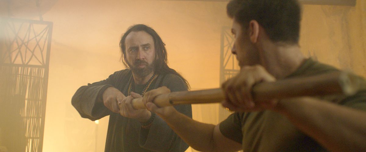 Nicolas Cage, con lunghi capelli arruffati, affronta Alain Moussi mentre afferrano le estremità opposte di un bastone in Jiu Jitsu