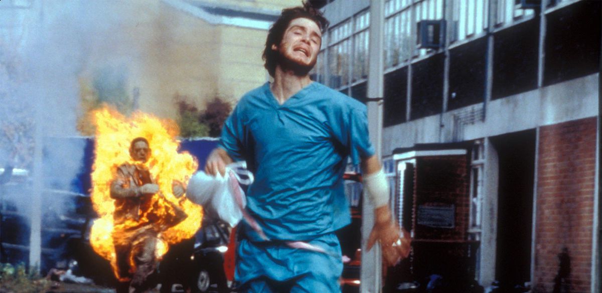 A man in scrubs runs away from a zombie on fire