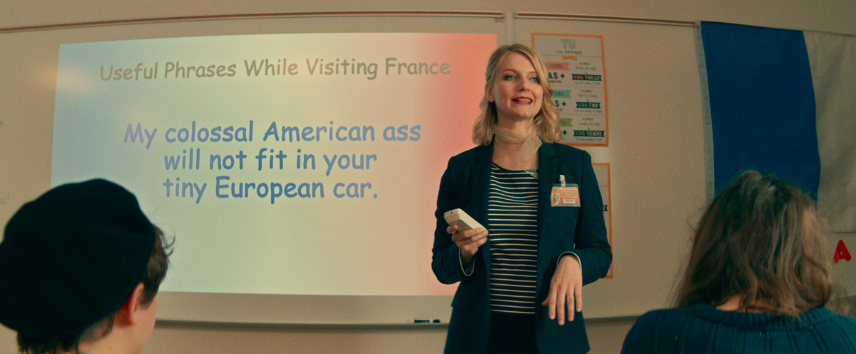 un insegnante di francese davanti a una diapositiva powerpoint che dice che il mio colossale culo americano non si adatterà alla tua minuscola macchina europea