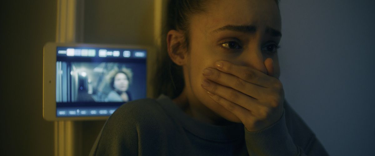 Sofia Carson gasps in horror with.a security camera feed behind her in Songbird