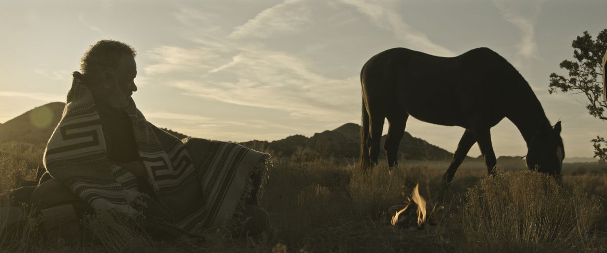 Kidd (Tom Hanks) coperto da una coperta giace in un campo guardando il suo cavallo mentre il sole tramonta in News of the World
