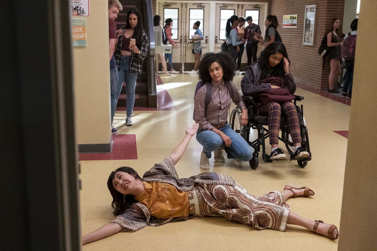 Ramona Young flops on the floor in the school hallway as Lee Rodriguez and Maitreyi Ramakrishnan look on in Never Have I Ever