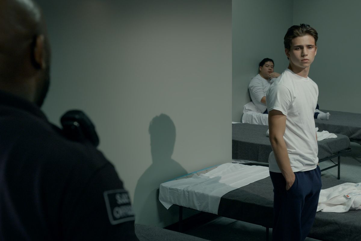 Robbie Keene (Tanner Buchanan) in piedi accanto alla sua branda della prigione con le mani in tasca, guardando lontano da una guardia in primo piano.