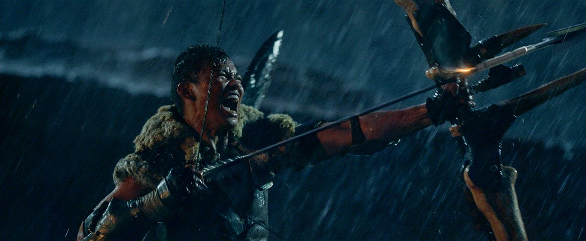 Tony Jaa, urlando sotto la pioggia e brandendo il suo arco gigante in Monster Hunter