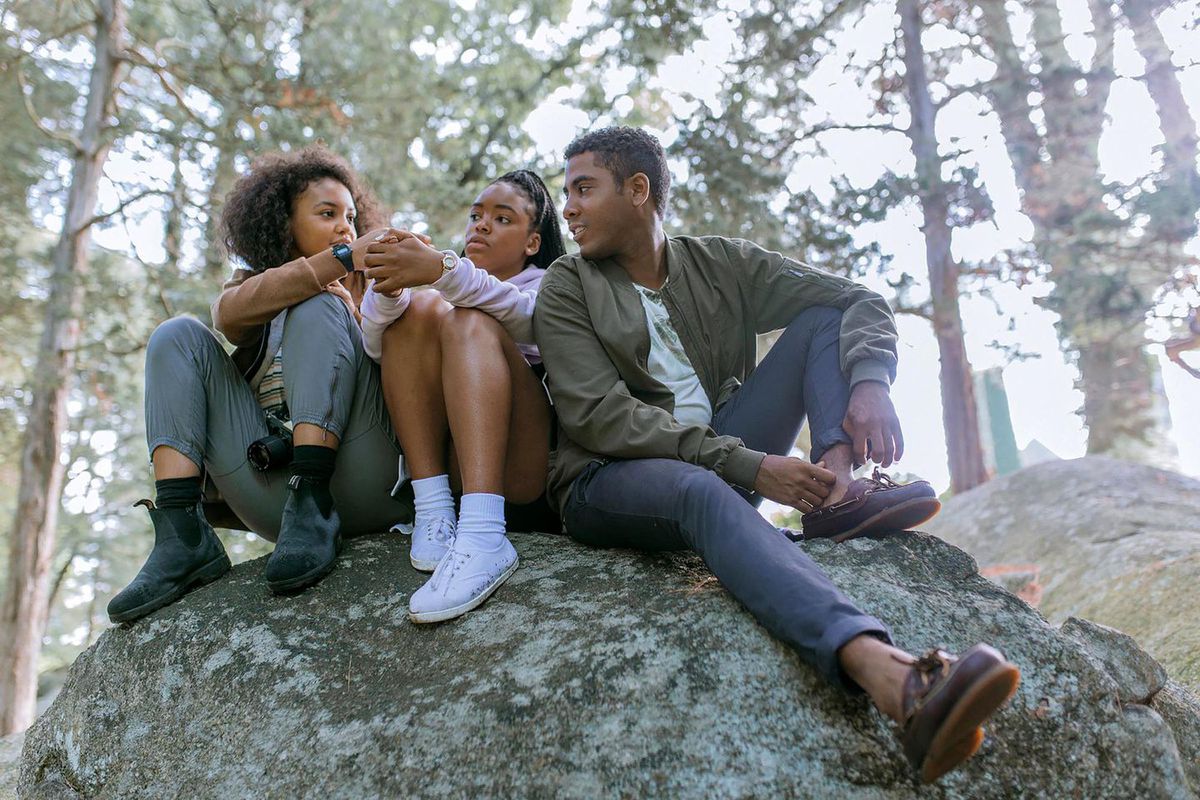 Celeste O’Connor, Lovie Simone, and Jharrel Jerome sit on a rock in a park