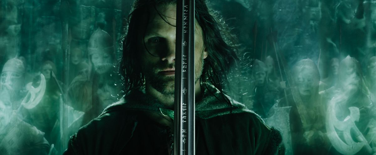 Aragorn stands with his sword in front of his face, ready to lead the green-glowing army of the dead in Lord of the Rings