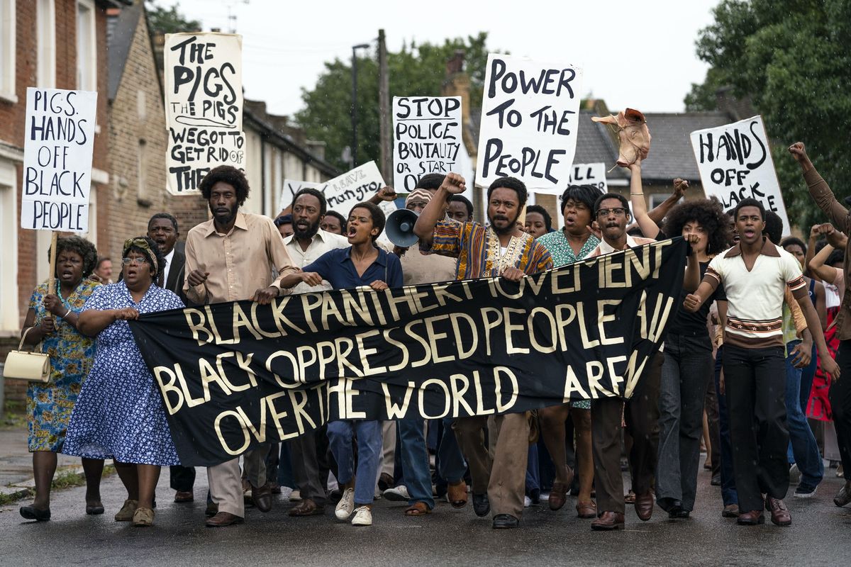 Un folto gruppo di manifestanti neri porta uno striscione della Pantera Nera nel film Mangrove della serie Small Axe di Steve McQueen