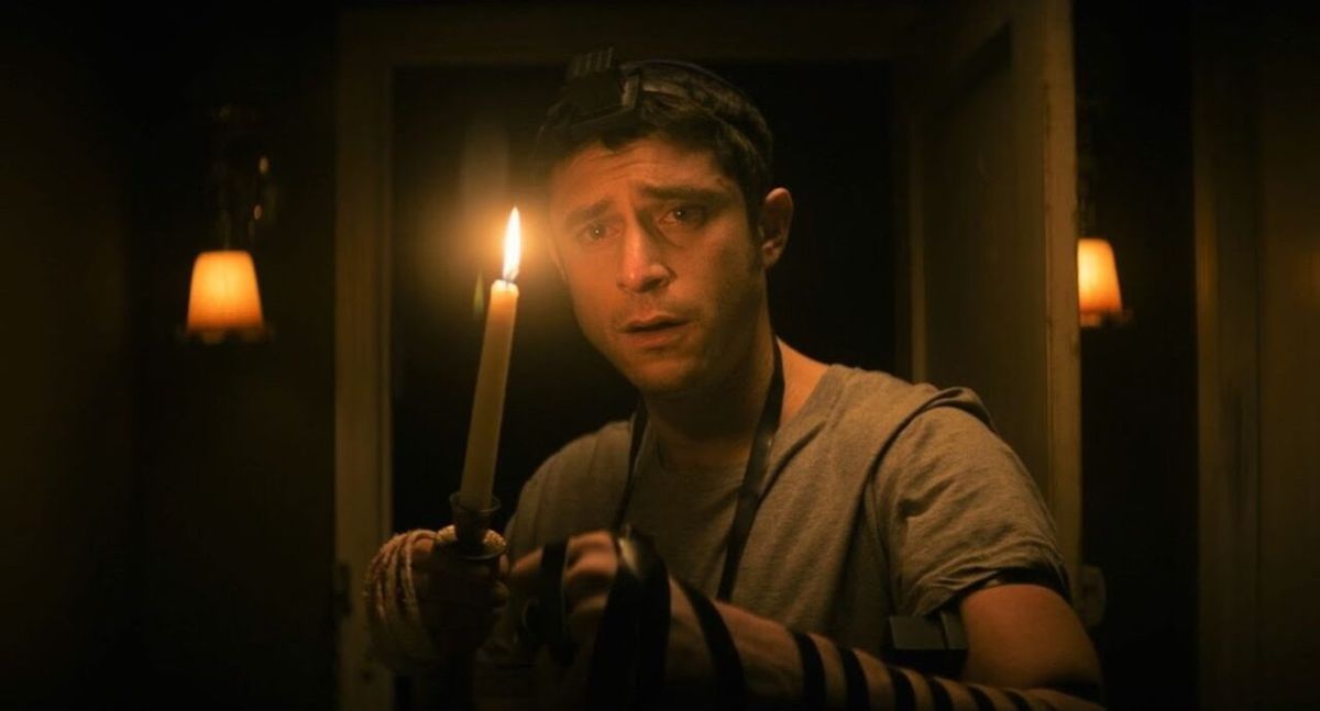 Dave Davis as Yakov holds a candle in a dark hallway in Keith Thomas’ The Vigil.