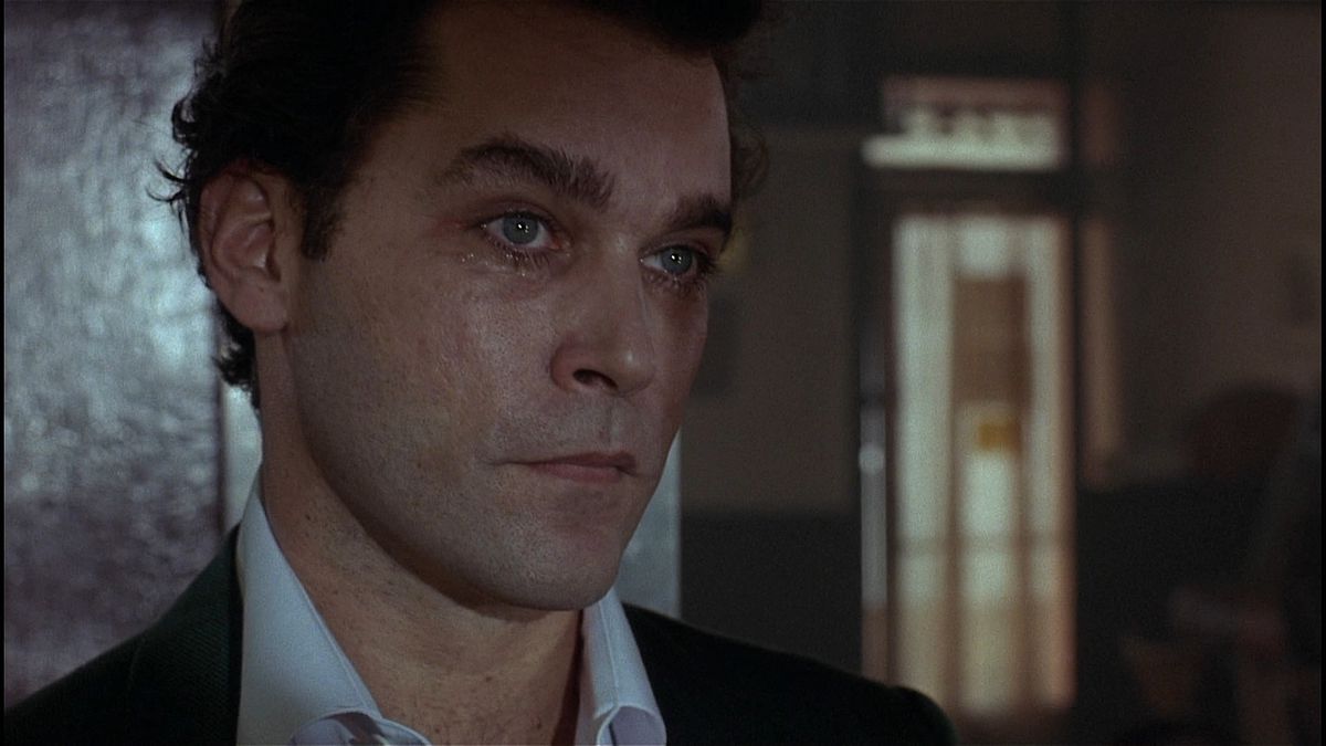 Un uomo sudato e imbronciato (Ray Liotta) con un occhio livido in piedi contro un muro scuro.