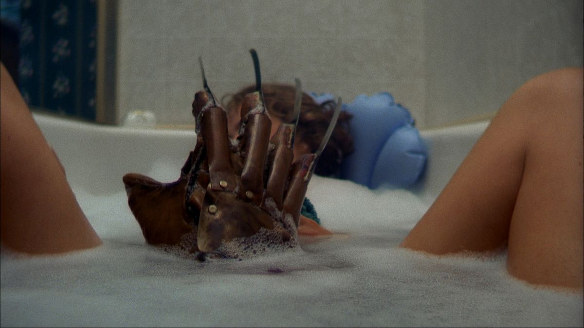 Freddy Krueger’s razor claw emerges from the bathtub between two female legs in A Nightmare on Elm Street 