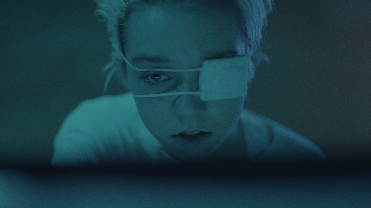 A closeup of Julia Sarah Stone wearing an eyepatch in soft blue light in Come Away